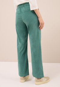 Zelené kordové kalhoty širokého střihu s elastickým pasem, zadními kapsami a hladkým povrchem, spárované s béžovými teniskami.