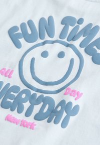 Usmívající se obličej s textem "FUN TIME" nahoře a "EVERYDAY" dole modře, s "all Day" a "New york" v menším růžovém textu na bílé látce.