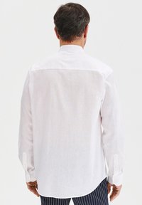 Biała koszula z długim rękawem, wykonana z lekkiego materiału, z klasycznym kołnierzykiem, zaokrąglonym dołem i mankietami na guziki, o prostym wzorze.