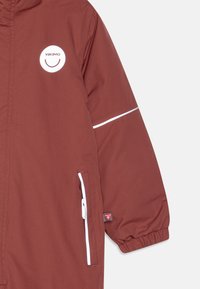 Casaco de crianças na cor bordeaux com capuz, logótipo branco, detalhes refletivos, bolsos com fecho e punhos elásticos para um ajuste seguro.
