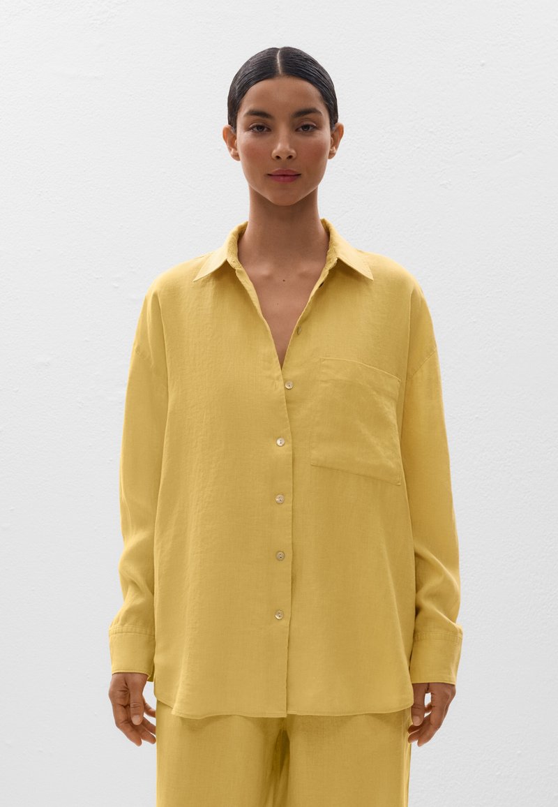Chemise jaune à boutonner en tissu léger, dotée d'un col, de manches longues et d'une poche poitrine. Texture lisse et coupe décontractée.