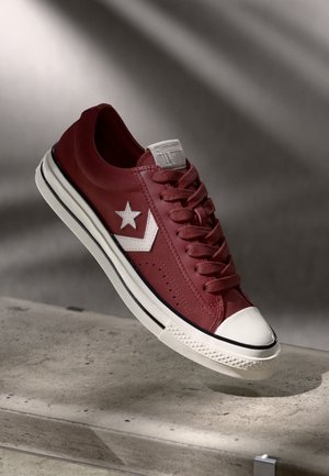 Røde lærersneakers med hvit stjerne-logo, teksturert overflate, rund tåhette og hvit mellomsåle med svarte striper og snøringer.