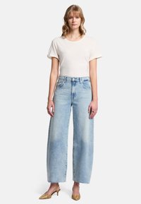 Jasno beżowa koszulka z krótkim rękawem w połączeniu z jasnoniebieskimi, wysokimi spodniami o szerokich nogawkach, z postrzępionymi brzegami i luźnym krojem.