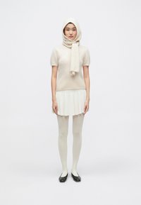 Bluză din lână deschisă la culoare, cu mâneci scurte, asortată cu o fustă mini plisată, ciorapi opaci și balerini negri. Modelul poartă o eșarfă asortată.