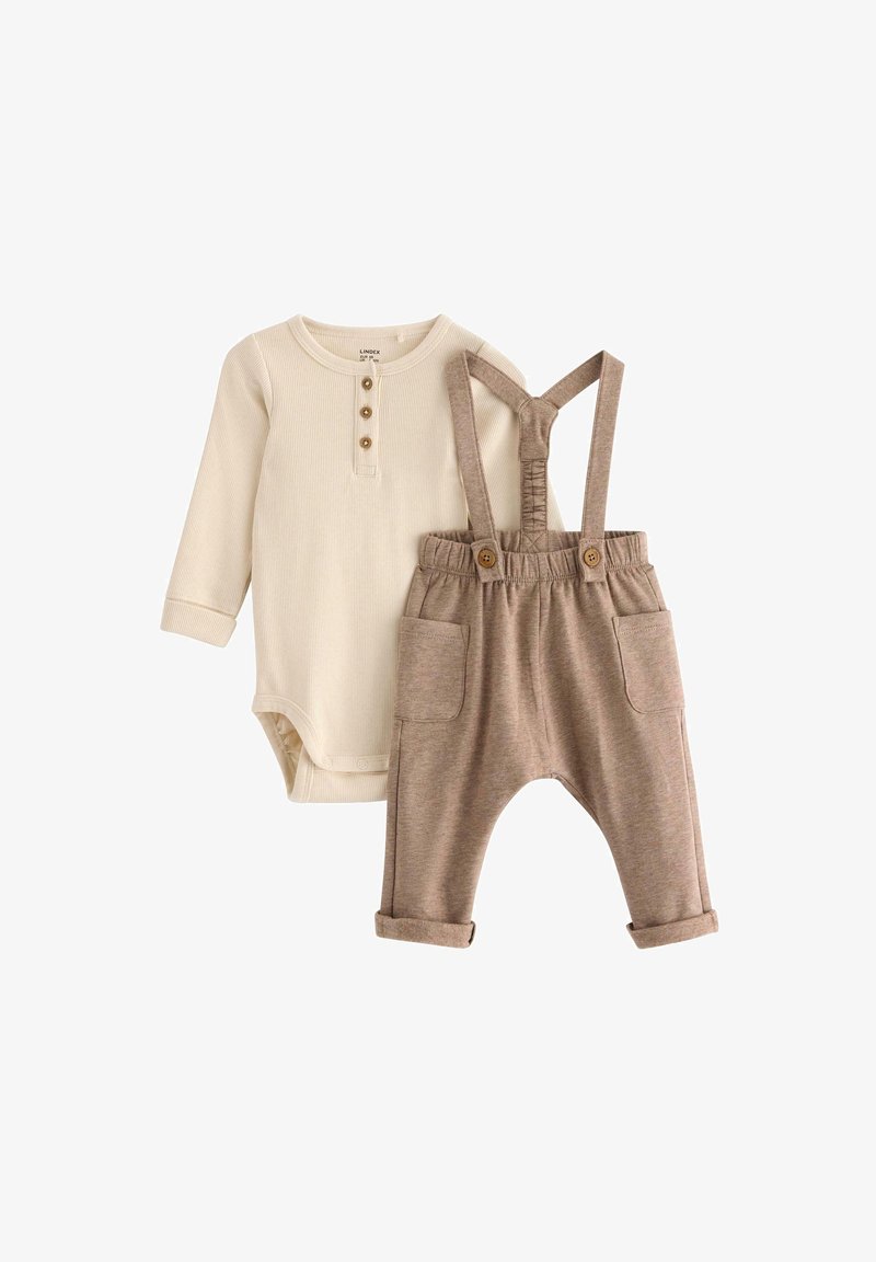 Krémový bodysuit s dlouhým rukávem a třemi knoflíkovými průramky, doplněný hnědými laclovými kalhotami s ohrnutými manžetami a předními kapsami.