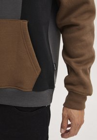 Grijze, zwarte en bruine hoodie met een pouch pocket, ribgebreide manchetten en een label op de zoom. Zachte stoftextuur.