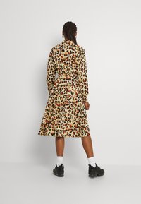 Vestido de padrão de leopardo em bege, com mangas longas, um laço na cintura e uma saia evasé. O material parece suave com um brilho sutil.