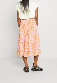 Blommig kjol i rosa och orange nyanser med en rynkad midja. Lättviktig tyg med en flödande siluett. Svarta remsandaler.