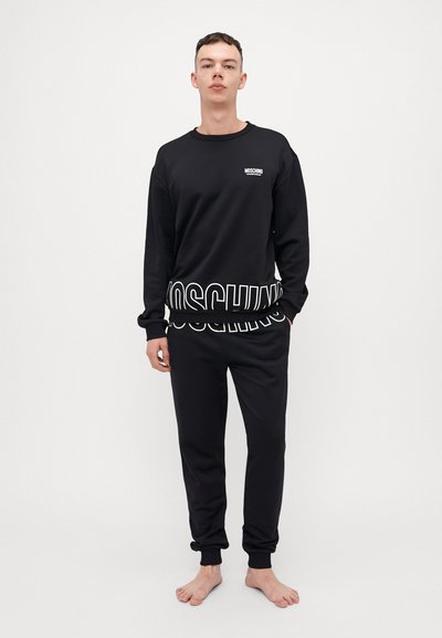 Black cotton sweatshirt and pants set featuring a large "Moschino" logo in white. Soft texture and ribbed cuffs on sleeves and ankles.