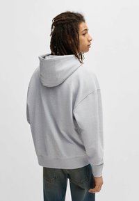 Light gray hoodie, cotton blend, oversized fit, features a large hood, ribbed cuffs, and hem, worn with blue denim jeans.