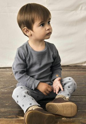 Camisa de manga larga de rayas gris combinada con pantalones grises claros que tienen un patrón floral. Zapatos marrones con suelas texturizadas completan el conjunto.