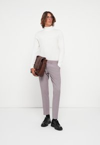 Valkoinen poolopaita, vaaleansiniset slim fit -housut, mustat kengät ja ruskea nahkainen viestintälaukku. Malli seisoo yksinkertaista taustaa vasten.