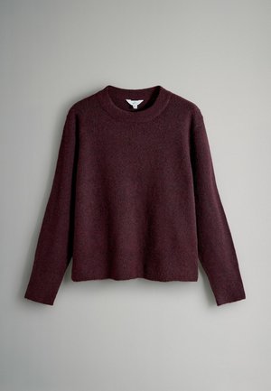 Vīna sarkana džemperis ar apaļu kakla izgriezumu, garām piedurknēm un mīkstu, teksturētu adījumu. Raksturīga brīvs piegriezums un malu, kas sasniedz vidukli.