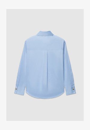 Chemise bleu clair à manches longues avec une texture douce, col structuré, pli dans le dos, et poignets à boutons.