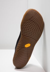 Czarna podeszwa buta z teksturowanej gumowej powierzchni, z logo Vibram w kolorze żółtym. Projekt zawiera wzór kratki zapewniający przyczepność.