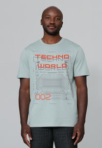 Licht teal kortekorte t-shirt met een grafische print in grijs en oranje. Heeft een ronde halslijn en een zachte textuur.