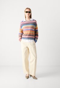 Mehrfarbiger gestrickter Pullover mit horizontalen Streifen, cremefarbene Hose und metallische spitze Absätze. Begleitet von dunklen Sonnenbrillen.