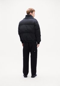 Black padded jacket with a wide collar, ribbed cuffs, and hem. Paired with loose-fitting black cargo pants and flat black shoes.