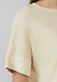 Licht beige kortarm top gemaakt van katoen; heeft een ronde hals en opgerolde mouwen met zichtbare stikdetails.