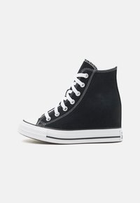 Svarta kanvas hög-top sneakers med vita snören, gummitåskydd och vit sula med två svarta ränder längs nederkanten.