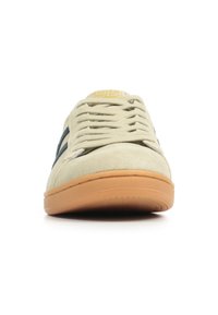 Beige suède sneaker met tan rubberen zool, groene accenten en platte veters. Rondneus en gestikte details op het bovenwerk.