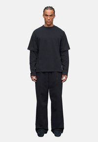 Schwarzes Baumwoll-Oversized-T-Shirt mit kurzen Ärmeln, über einem Langarmshirt getragen, kombiniert mit schwarzen weiten Sweatpants.