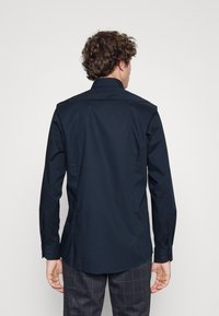 Marineblauwe langsl sleeveshirt met een puntige kraag, knoopmanchetten en een gladde stofstructuur. Heeft een getailleerde pasvorm en een rug yoke-detail.