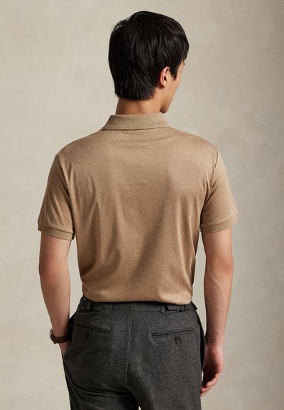 Brun polotrøye med korte ermer og krage, kombinert med mørkegrå bukser som har baklommer og beltehemper.