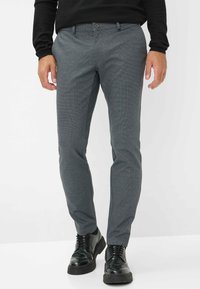 Pantaloni grigi con motivo, realizzati in tessuto leggero, con vestibilità slim, chiusura a bottone e abbinati a scarpe nere.