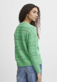 Pull en tricot vert avec un design texturé, featuring des rayures ajourées et un ourlet côtelé. La coupe est décontractée, avec des épaules tombantes.
