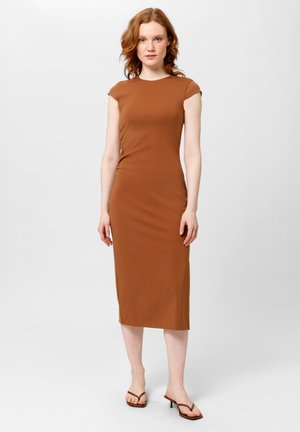 Robe midi marron ajustée avec des manches courtes, texture lisse et un détail de fronce sur le côté. Associée à des sandales à talons fins.