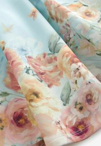 Tissu bleu clair avec un motif floral doux comprenant de grandes roses roses, pêche et crème ainsi que des feuilles vertes.