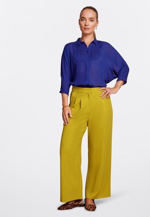 Blusa azul de manga larga con detalle de pliegues en el frente, combinada con pantalones de pierna ancha verde oliva y bailarinas de estampado de leopardo.