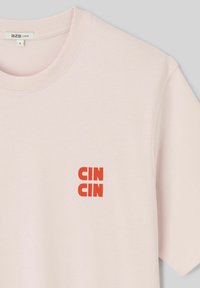 T-shirt rose clair à manches courtes avec col rond et texte rouge vif « CIN CIN » imprimé sur la partie gauche de la poitrine.