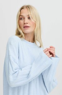 Hellblauer, gestrickter Pullover mit lockerer Passform. Verfügt über eine breite Rippstruktur und überschnittene Schulternaht. Lange, weite Ärmel.