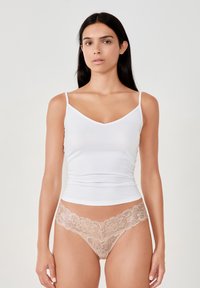 Weißes, enges Tanktop mit dünnen Trägern und V-Ausschnitt, kombiniert mit hellbeiger Spitzenunterwäsche mit floralen Mustern und gewellten Kanten.
