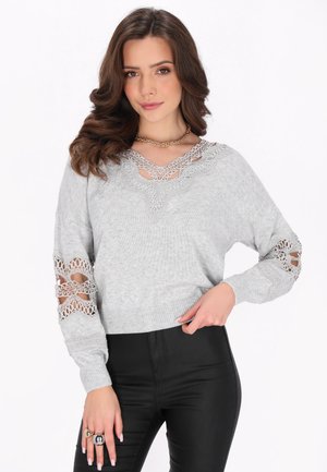 Maglione grigio a maglia con un accento in pizzo attorno al collo e dettagli a disegno sulle maniche, con orlo aderente. Pantaloni in pelle nera.