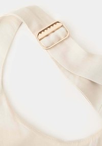 Sangle en tissu beige avec une boucle rectangulaire dorée dotée d'une barre intérieure dentelée pour une fixation ajustable.
