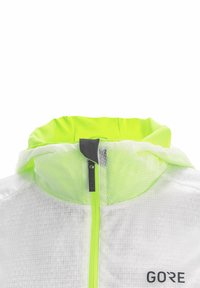 Chaqueta cortavientos blanca transparente con un interior de color verde neón en el cuello, cremallera frontal y logotipo negro en la parte inferior derecha. Textura en cuadrícula visible.