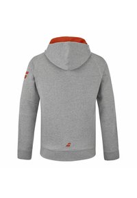 Haut à capuche gris avec une doublure intérieure rouge. Dispose de manches raglan, d'un logo rouge sur l'épaule gauche et de poignets et d'un ourlet côtelés.