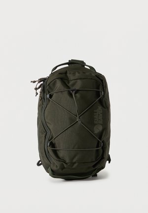 Tummanvihreä suorakaiteen muotoinen reppu, jossa ulkoinen joustinnyöri, vetoketjutaskut ja yläkahva, seisoo pystyasennossa yksinkertaisella taustalla.