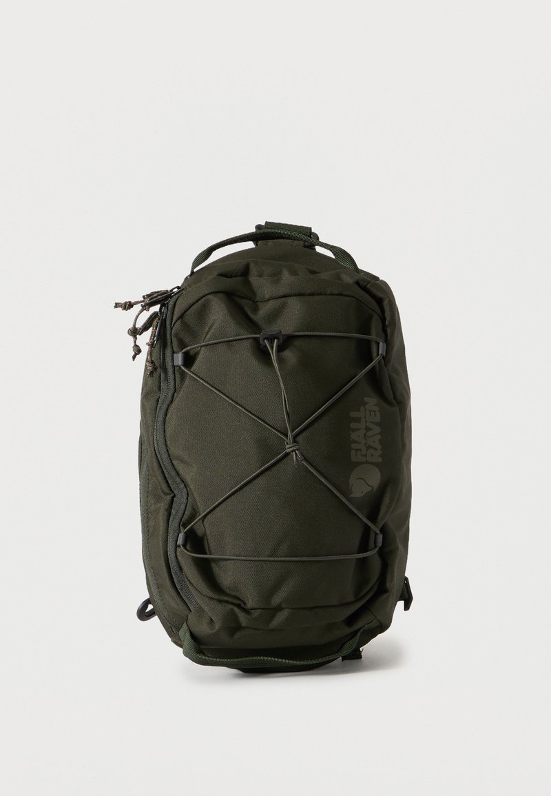 Σκούρο πράσινο ορθογώνιο σακίδιο με εξωτερικό ελαστικό κορδόνι, τσέπες με φερμουάρ και επάνω χερούλι, όρθιο σε απλό φόντο.