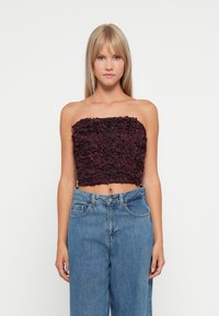 Burgundy strapless crop top with a textured floral design, paired with high-waisted blue denim jeans. Simple and fitted silhouette.
