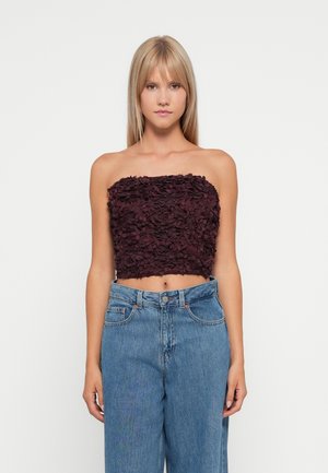 Burgundy strapless crop top with a textured floral design, paired with high-waisted blue denim jeans. Simple and fitted silhouette.