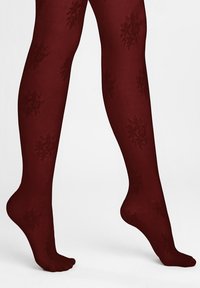 Nogi ubrane w bordowe rajstopy z subtelnymi wzorami płatków śniegu, stojące na palcach na jednolitym tle.