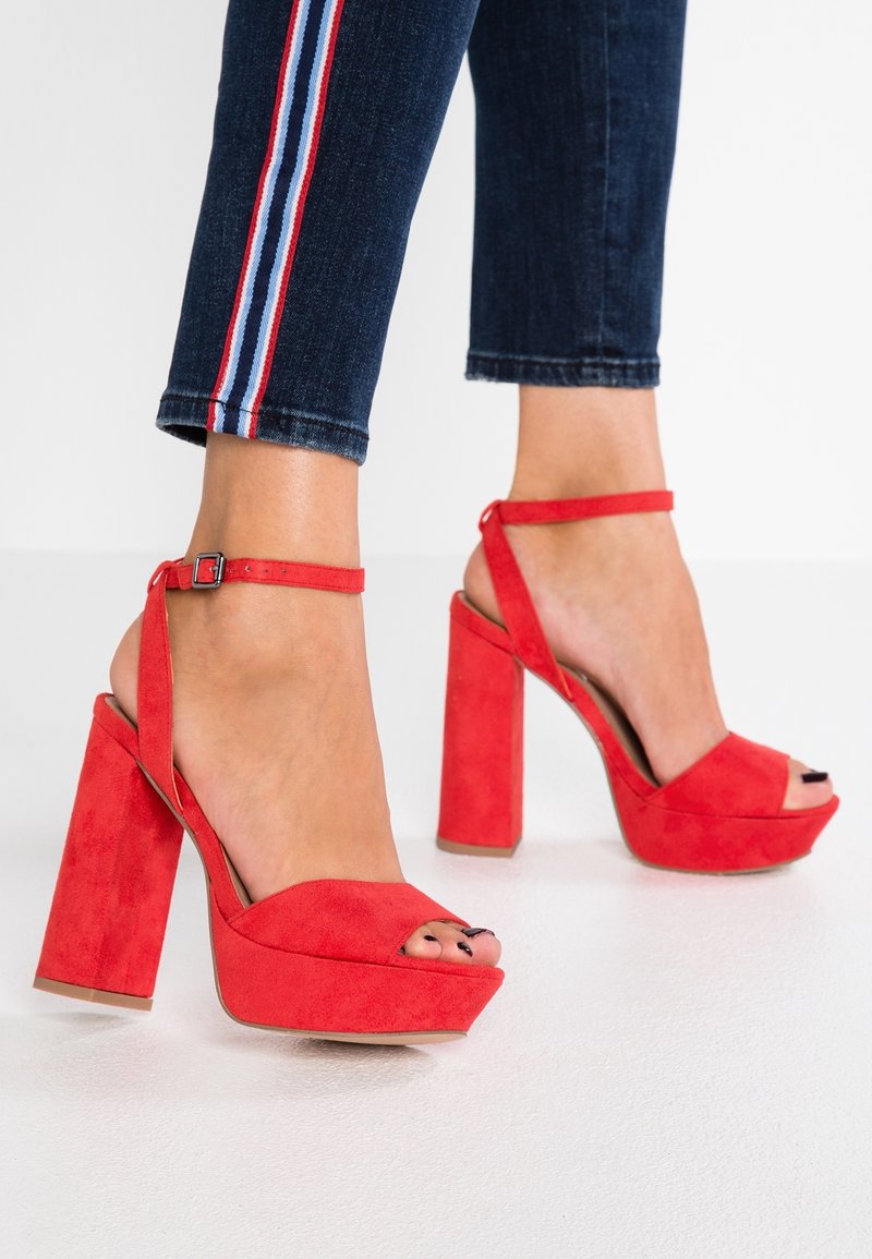 Sandales à talons hauts en daim rouge avec une plateforme, bout ouvert et lanière à la cheville. Présente un épais talon bloc et une texture lisse.
