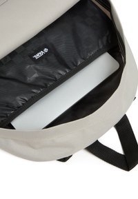 Mochila gris con forro interior negro que incluye un compartimento para portátil y una etiqueta de Vans. El tejido es resistente, con una textura suave y forma estructurada.