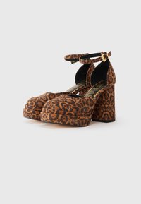 Løveprikkede plattformhæle med bred blokhæl og ankelrem, lavet af blødt stof med en struktureret overflade. Guldfarvet spænde detaljer.