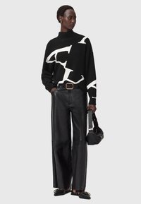 Czarny sweter z dzianiny z białym abstrakcyjnym wzorem, w połączeniu z szerokimi czarnymi skórzanymi spodniami, czarnymi butami i czarną torebką.