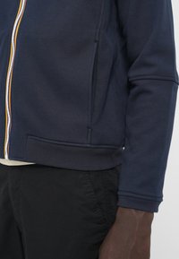 Marineblå lynlås-sweater med ribbet kanten og ærmer. Har en flerfarvet lynlås og sidelommer. Slankt, tekstureret stof.